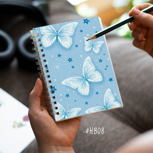 Notebook with butterfly design held by a person with a pencil, on a blurred background.