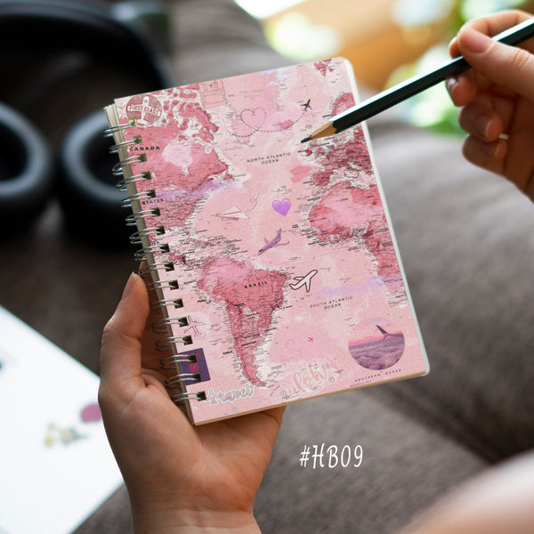Person holding a pink notebook with world map design on a desk.