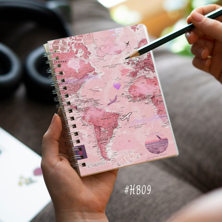 Person holding a pink notebook with world map design on a desk.