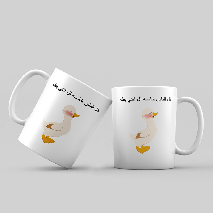 Two white mugs with a duck illustration and Arabic text on a light gray background
