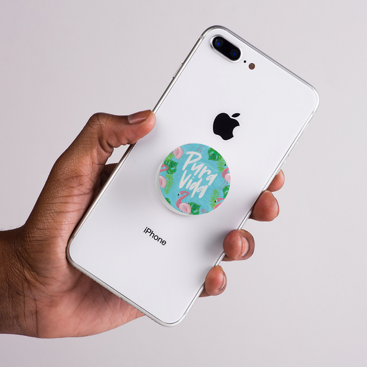 Hand holding a white iPhone with a floral 'Para Vida' pop socket on the back