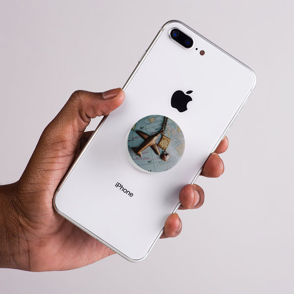 Hand holding a white iPhone with a map pop socket on the back against a light gray background
