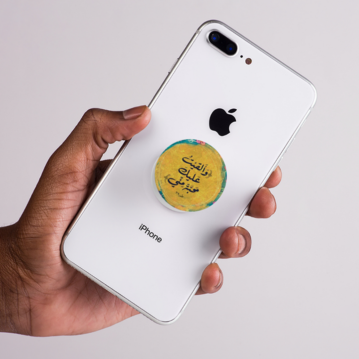 Hand holding a white iPhone with a colorful arabic quote pop socket on the back