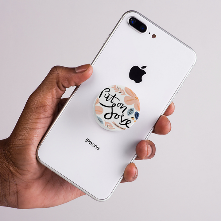 Hand holding an iPhone with a pop socket on a light gray background