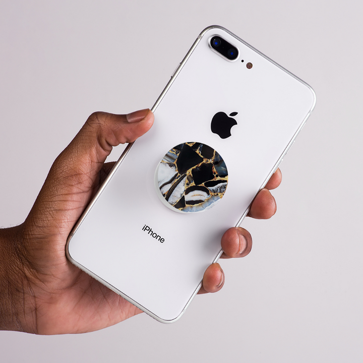 Hand holding a white iPhone with a marble-patterned pop socket on a light gray background