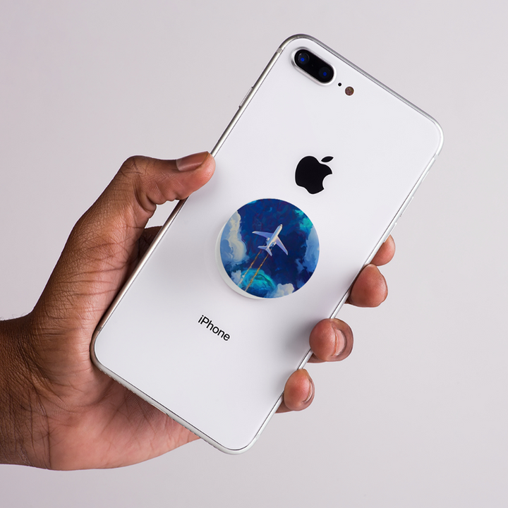 Hand holding a white iPhone with a blue sky and airoplane circular popsocket  on a light gray background