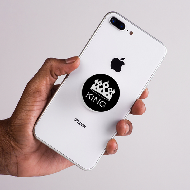 Hand holding a white iPhone with a 'King' pop socket on the back