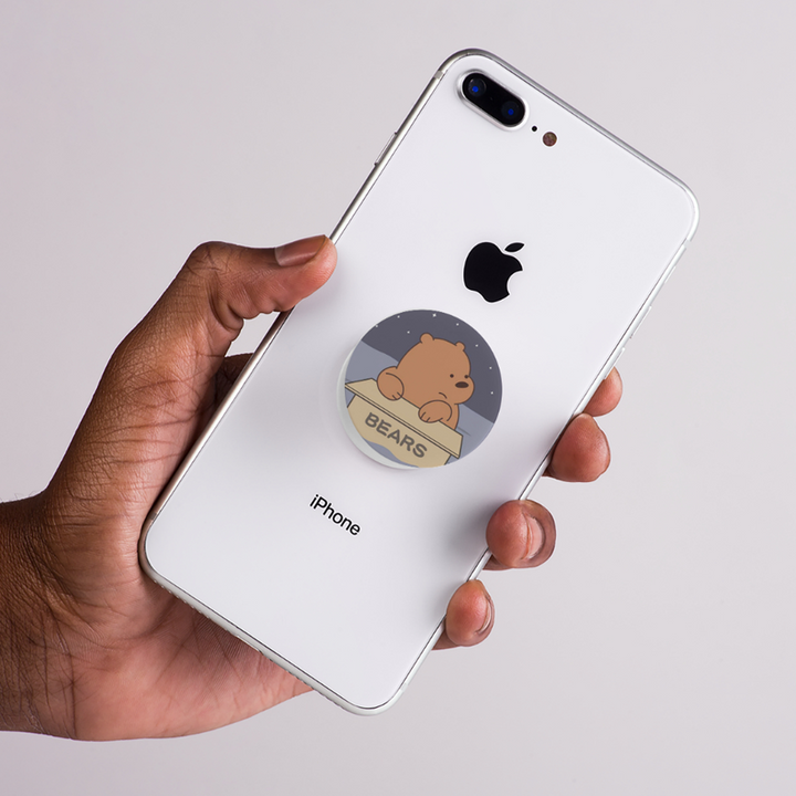 Hand holding an iPhone with a PopSocket featuring a bear design on a light gray background