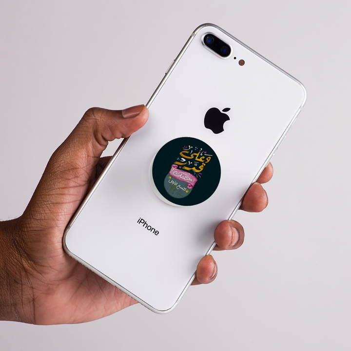 Hand holding a white iPhone with a colorful sticker on the back against a light gray background