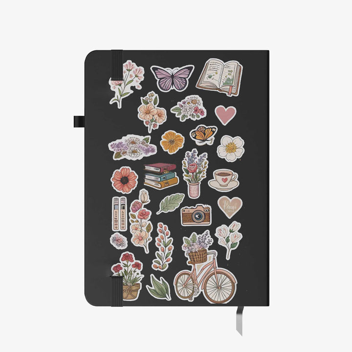 Hardcover notebook with black cover decorated in floral, butterfly, book, and coffee stickers for a cozy aesthetic

